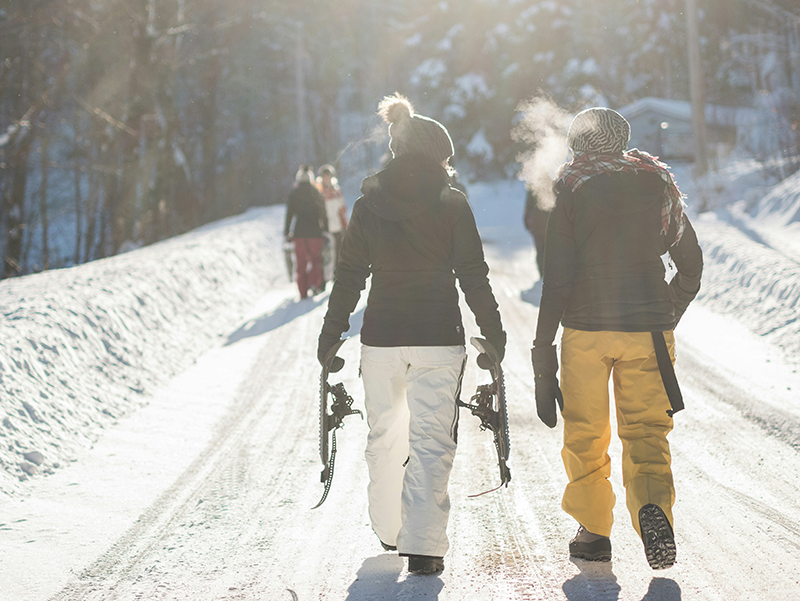 Si vedono due ragazze di spalle che infreddolite ma contente si avviano in un sentiero innevato con l'attrezzatura sportiva in mano.