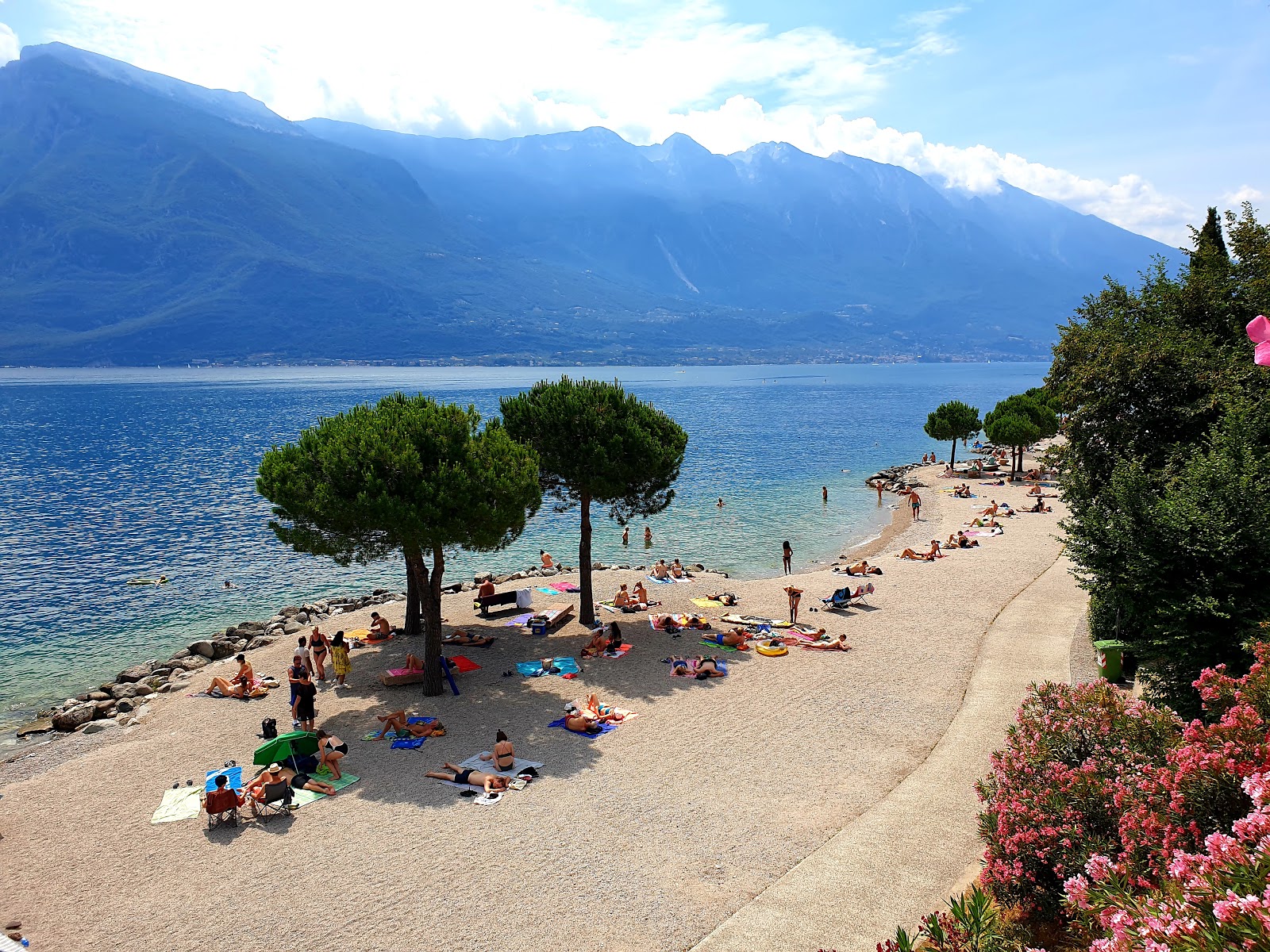 La spiaggia di Limone sul Garda è composta da una distesa di sassolini bianchi levigati. Questa distesa incontra le limpide acque del lago. Le montagne incorniciano l'orizzonte.