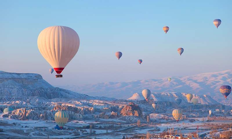 paesaggio lunare della Cappadocia, coperto da un velo delicato di neve. In cielo volano le caratteristiche mongolfiere colorate.
