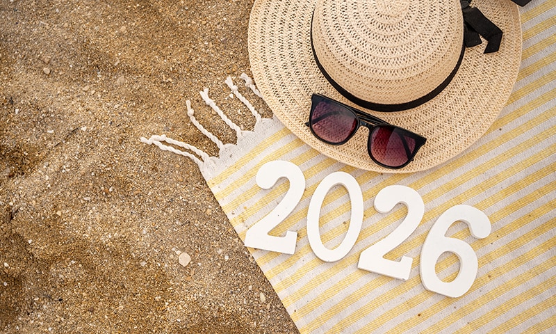 Cappello di paglia, occhiali da sole, asciugamano ed il numero 2026, sdistesi delicatamente su una spiaggia di sabbia dorata, un bel luogo per festeggiare Capodanno!